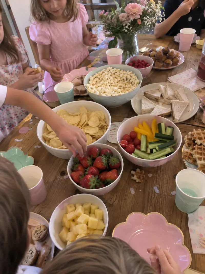 The party buffet from above: fruit, vegetables and small hands helping themselves.