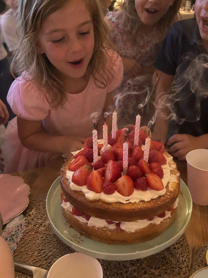 A little girl about to blow out the candles on her strawberry cake.
