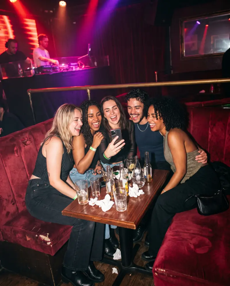 Five friends squeezed onto a club banquette look at a photo on a phone.