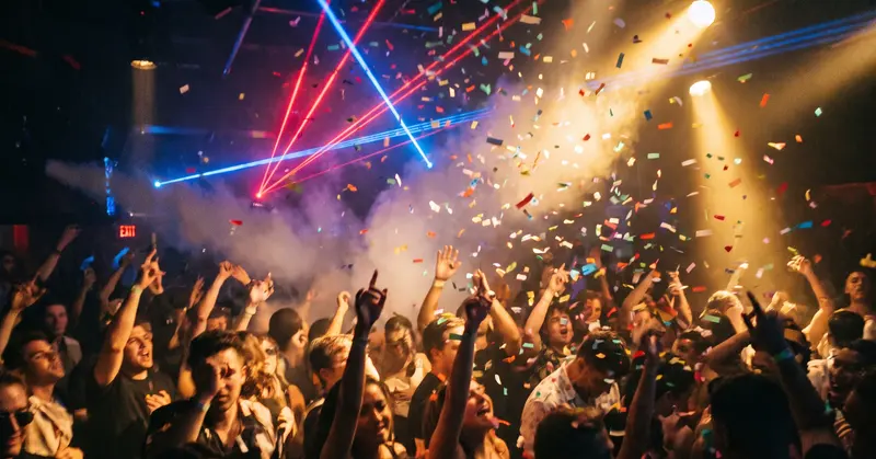 Confetti falls over a club dance floor, under laser lights.