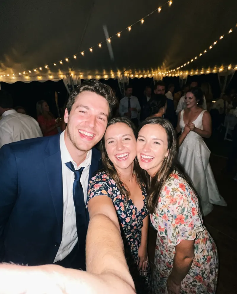 Three wedding guests laugh in a selfie on the dance floor, with the bride behind them.