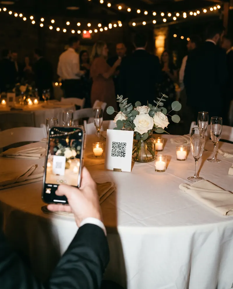 A guest scans the QR code on a table card with a phone, at a wedding table with flowers and candles.
