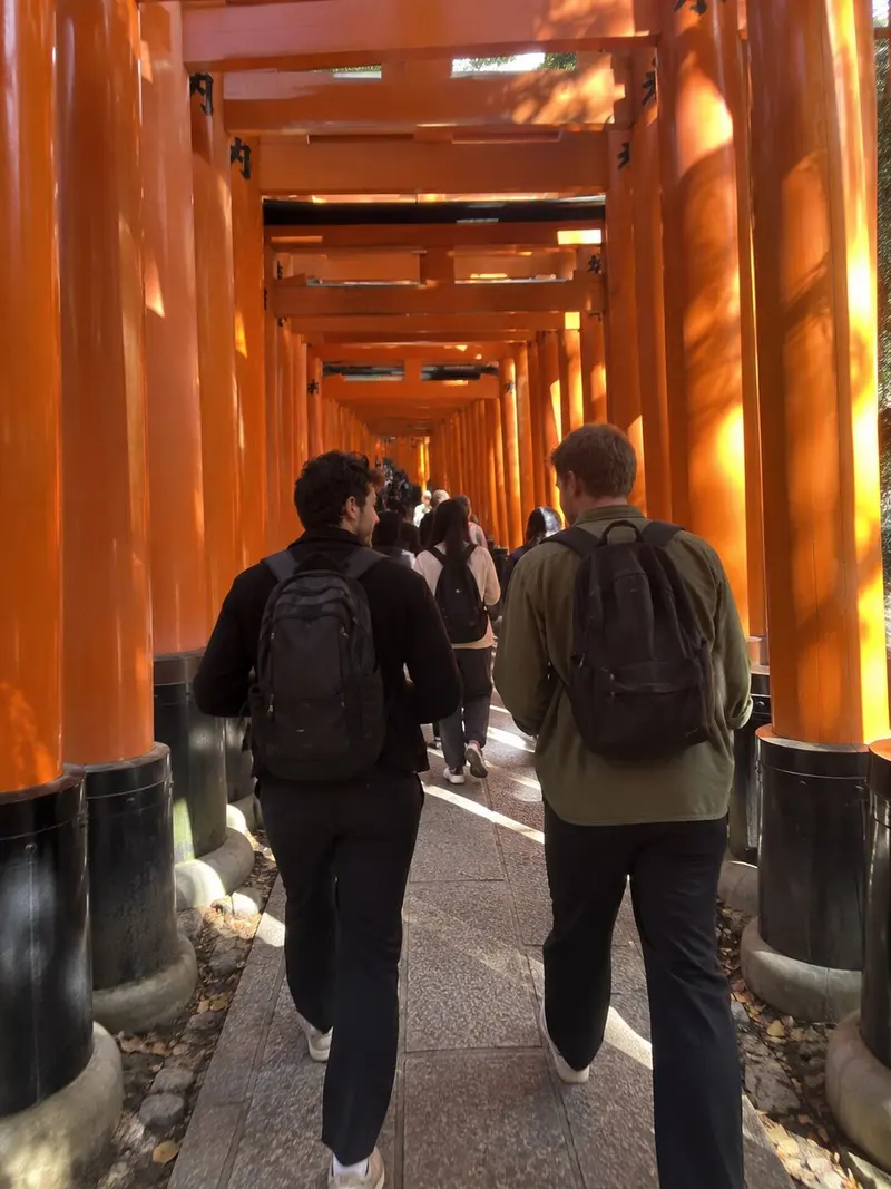 Two friends walk under the rows of orange torii gates in Kyoto.