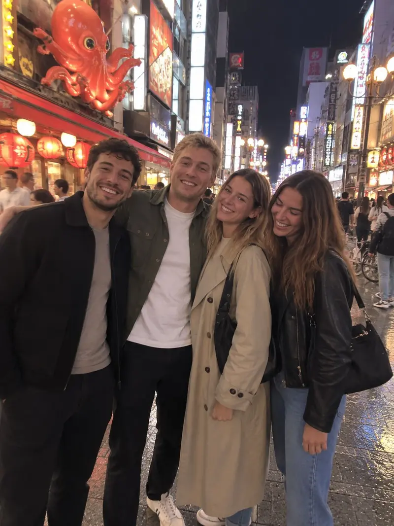 Four friends smile on a brightly lit street in Osaka at night.
