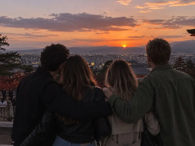 Four friends watch the sunset, arms around each other.
