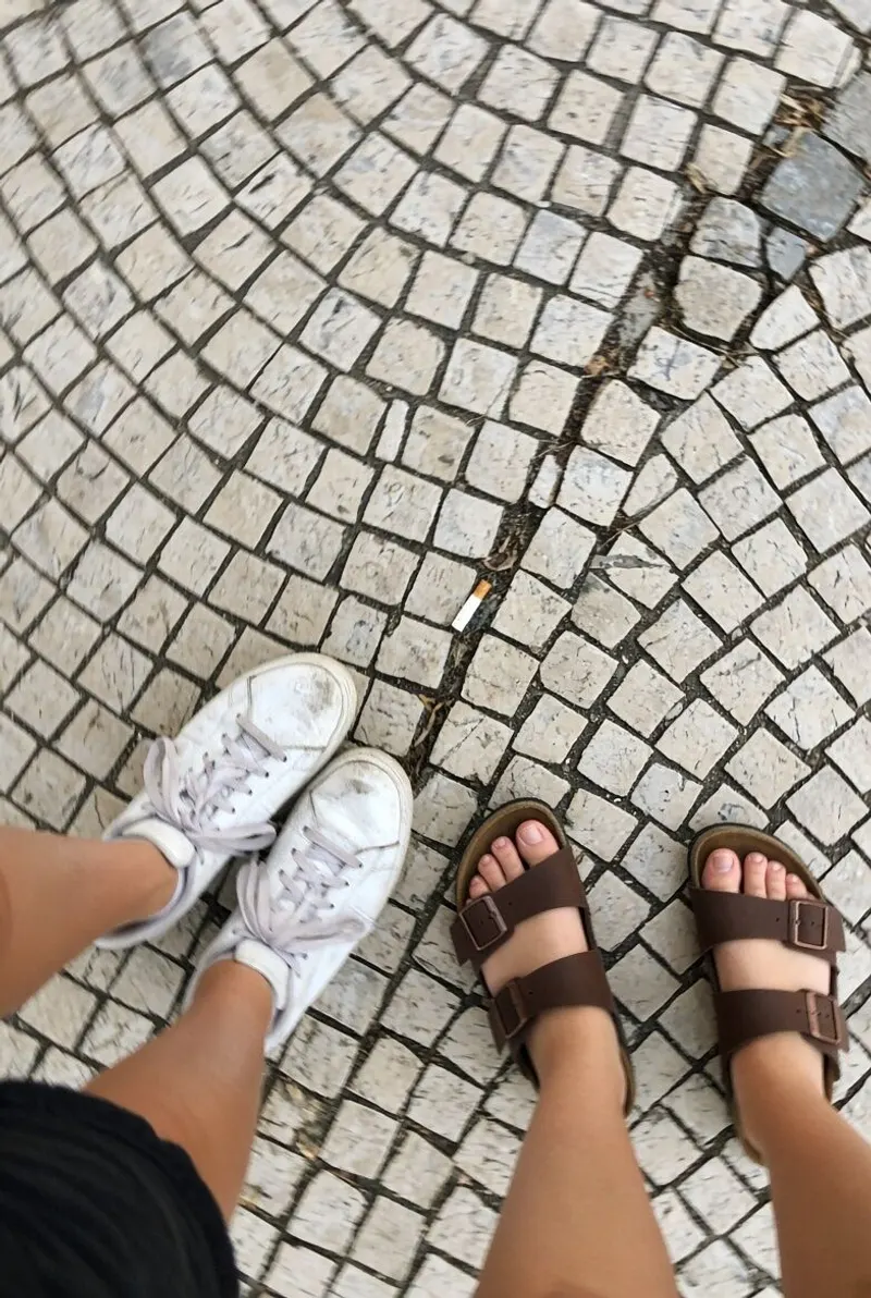 Two pairs of feet on Lisbon’s black and white paving stones.